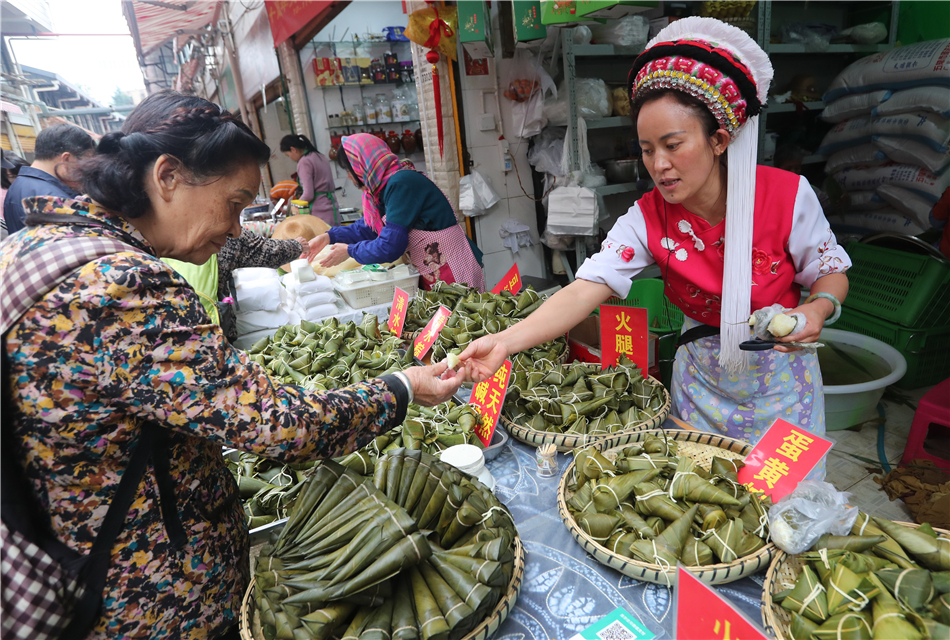 An elderly buys Zongzi from a girl wearing the Bai ethnic costume.